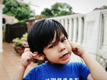 Close-up portrait of cute boy holding ears while standing outdoors