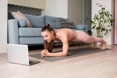 Workout class live streaming concept. woman doing plank online from laptop in living room. 