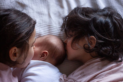 Upper view on heads of two girls kissing newborn sister lying on the bed