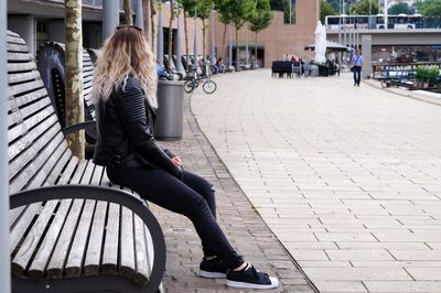 Rear view of woman sitting on sidewalk in city