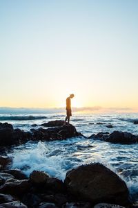 Rear view of man walking on beach against clear sky during sunset