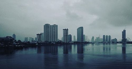 City at waterfront against cloudy sky