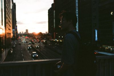 Man standing by railing on bridge in city during sunset
