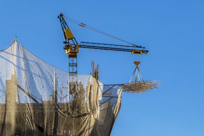 Low angle view of crane against clear blue sky