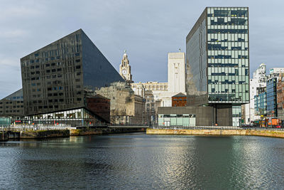 Modern buildings by river against sky in city