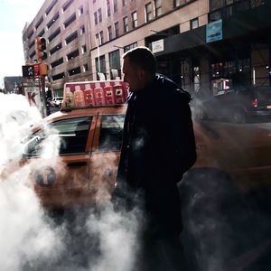 Mid adult man surrounded by smoke while standing against car on street