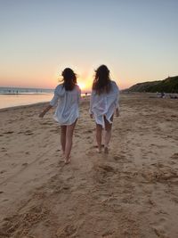 Rear view of women walking on beach during sunset