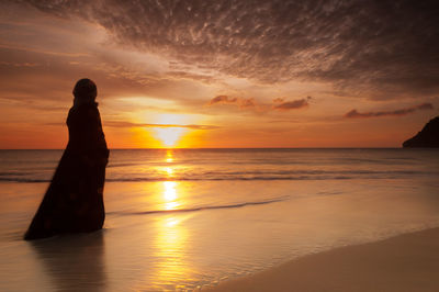 Silhouette man standing on beach against sky during sunset