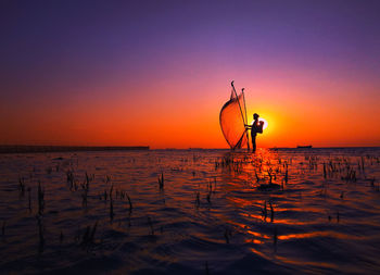 Silhouette man fishing by sea against clear sky during sunset