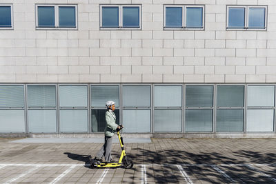 Young businesswoman riding push scooter in front of office building on footpath