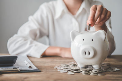 Midsection of businessman putting coin in piggy bank