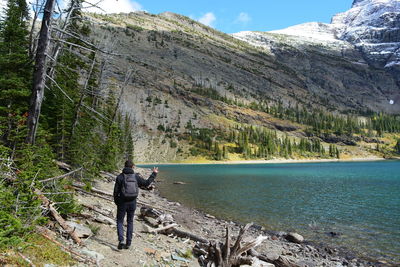 Rear view full length of hiker showing peace sign by lake at waterton lakes national park