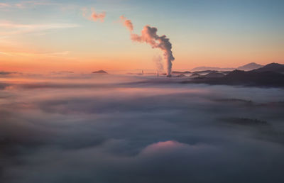 Smoke emitting from factory against sky during sunset