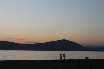 Silhouette people standing on beach against clear sky during sunset