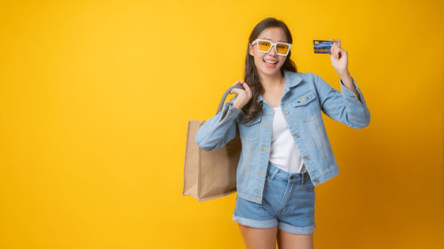 Portrait of smiling young woman against yellow background