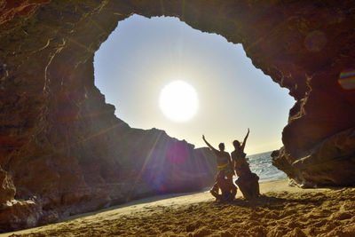 People standing on rock formations against bright sun