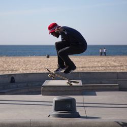 Man skateboarding on skateboard by sea against clear sky