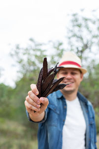 Man, farmer, worker holding in hands ripe brown carob pods during harvesting season in countryside