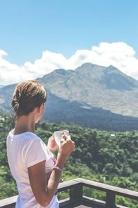 Woman holding coffee cup while looking at mountain