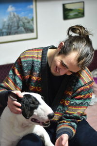 White caucasian male cuddling with a black and white bull terrier in a room