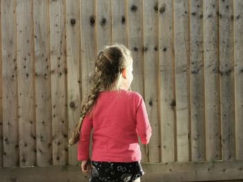 Rear view of a girl standing against wooden fence. 