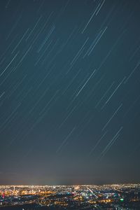 Star trails against sky over illuminated city at night