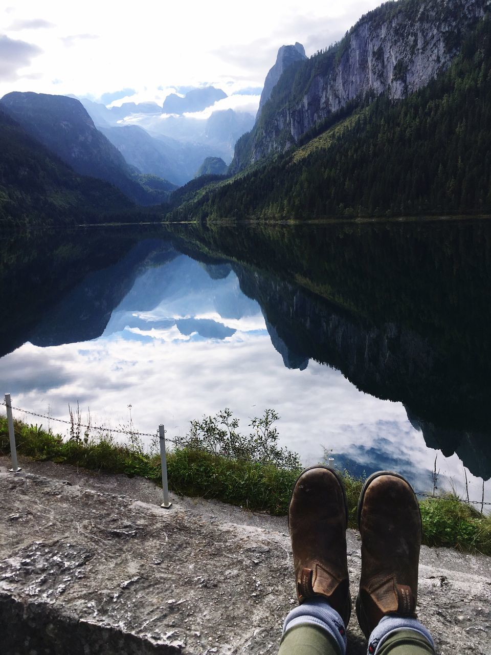 mountain, reflection, water, lake, tranquil scene, mountain range, tranquility, lakeshore, scenics, low section, standing water, beauty in nature, personal perspective, relaxation, idyllic, nature, person, majestic, tourism, non-urban scene, cloud, vacations, travel destinations, calm, outdoors, sky, remote, riverbank, lakeside, day