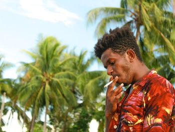 Portrait of young man looking away against trees