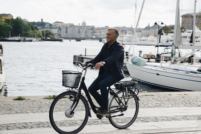 Full length of senior man riding bicycle on road by harbor
