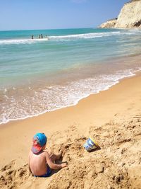 Rear view of boy sitting on sand at beach