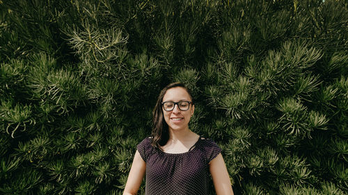 Smiling woman with eyes closed wearing eyeglasses against plants