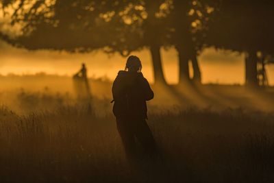 Silhouette man standing on field against sky during sunset