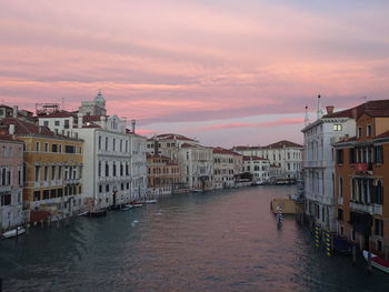 Canal passing through buildings against sky during sunset