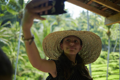 Teen girl wearing a big straw hat taking selfies using mobile phone