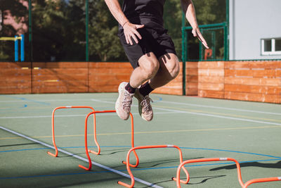 Blond boy in sportswear jumps over red obstacles to improve lower body dynamics