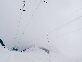 Low angle view of ski lifts over snow covered field against sky