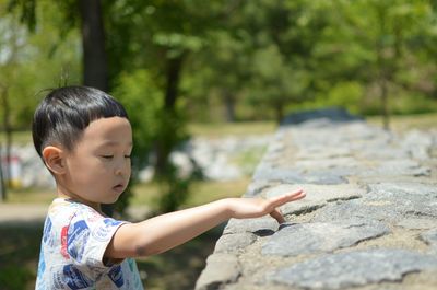 Boy touching retaining wall during sunny day