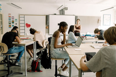 Junior high students studying while female teacher standing in classroom