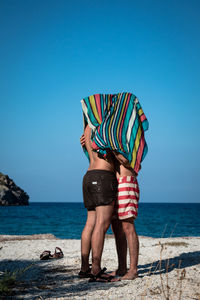 Gay men under towel romancing at beach against clear sky