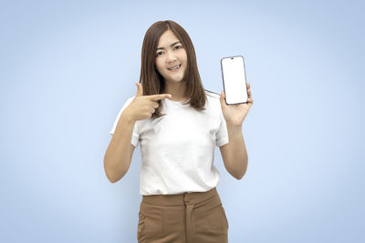 Portrait of smiling young woman using mobile phone against clear sky