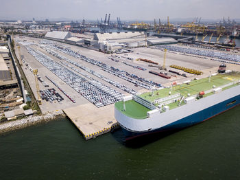 Aerial logistics commercial vehicles waiting to be load on to a car carrier ship at dockyard