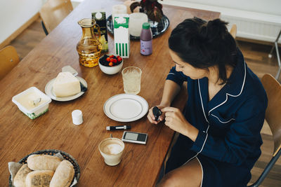 Woman checking diabetes while having breakfast on table at home