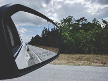 Reflection of trees on side-view mirror against sky