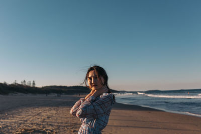 Portrait of woman standing at beach against clear blue sky