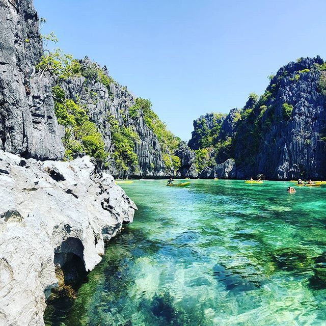 water, clear sky, tree, tranquility, scenics, tranquil scene, beauty in nature, blue, rock - object, nature, rock formation, waterfront, incidental people, copy space, mountain, idyllic, day, cliff, outdoors, sunlight