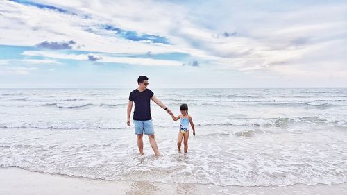 Full length of father and daughter standing on beach against sky