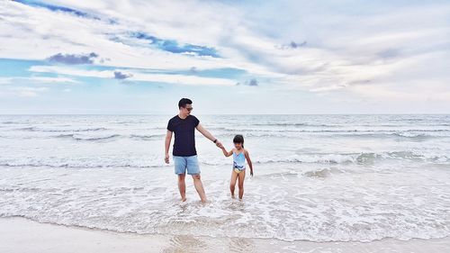 Full length of father and daughter standing on beach against sky