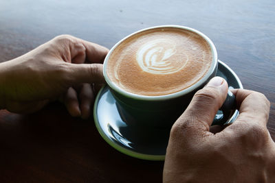 Close-up of hand holding coffee cup on table