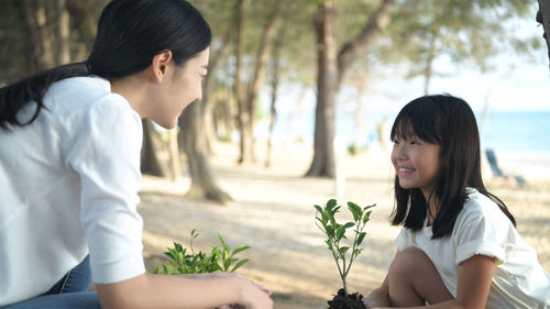 Happy girl with flowers on plant against trees