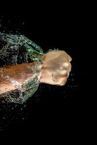 Cropped hand of man punching water against black background